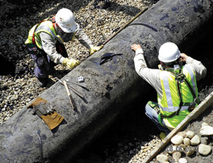 Technicians in protective equipment prepare pipe section before cutting and removing it from the Enbridge pipeline oil-spill site near Marshall, Mich. The segment was shipped to federal lab for analysis.